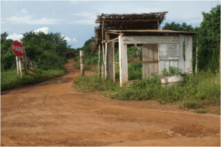 Dusty road with a shack: ‘Entrance is forbidden for people wearing helmets’, Serra Dourada Landless Encampment in Canaã dos Carajás, Eastern Amazonia – Rodrigo Castriota.