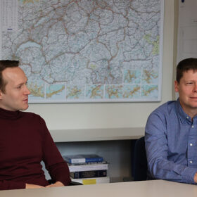 Arnór Elvarsson (l) und Bryan Adey (r) sprechen, am Tisch sitzend, hinter ihnen eine Schweizer Karte. © ETH Zürich
